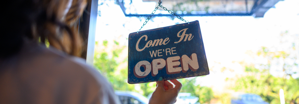 Portrait of business owner hanging an open sign on the door at a cafe.