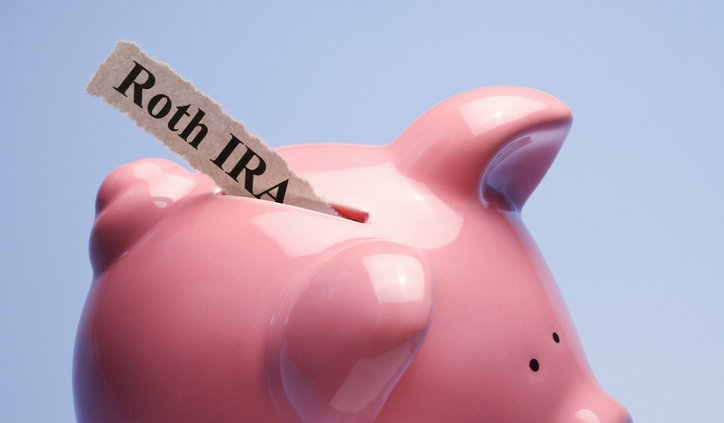 "Retirement" is printed on a torn piece of paper that is inserted into the coin slot of a pink piggy bank against a blue background.
