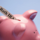 "Retirement" is printed on a torn piece of paper that is inserted into the coin slot of a pink piggy bank against a blue background.